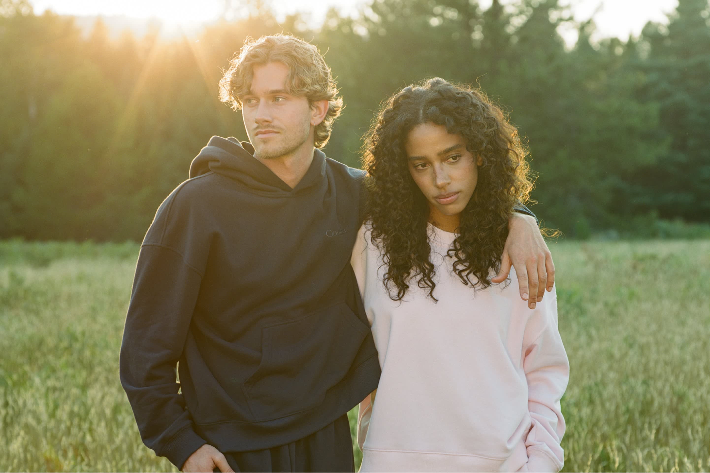 Two people standing in a sunlit field wearing Comfrt hoodies